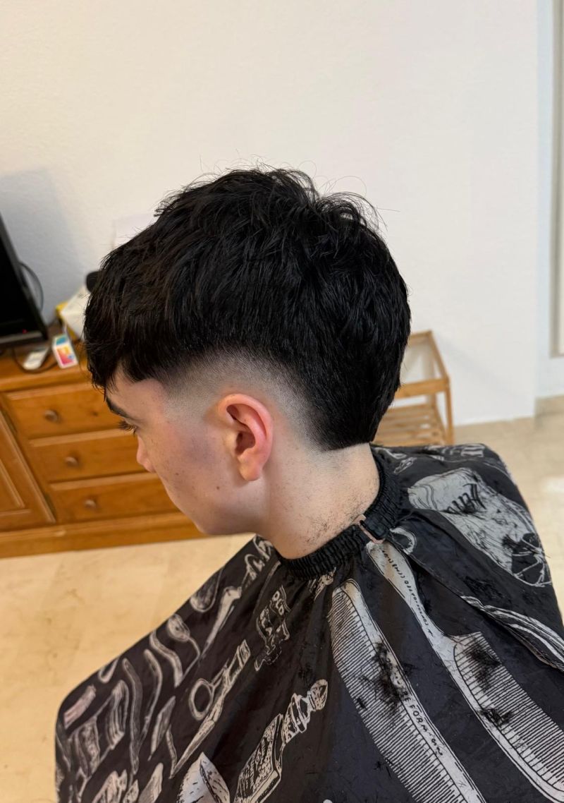 Corte texturizado de pelo negro con drop fade y flequillo despuntado sobre fondo claro.